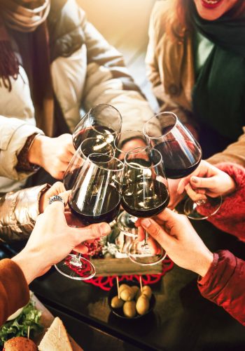 Happy friends group wearing winter clothes celebrating with red wine glasses